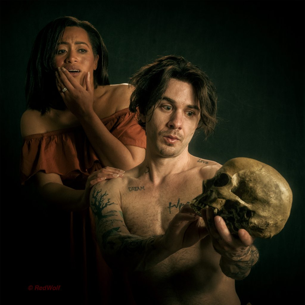 Image of an contemporary American man holding a skull in the style of Hamlet, with a woman, Ophelia, standing behind him.